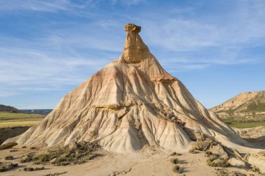 İspanya 'nın Bardenas Reales kentindeki kurak araziden bej yamaçlı dramatik bir büyü yükseliyor. Güneş ışığı keskin gölgeler bırakır, engebeli dokuları ve açık mavi gökyüzünün altındaki katmanlı toprağı ortaya çıkarır..