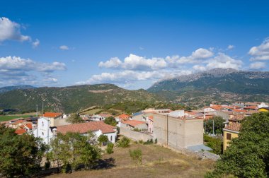 Orgosolo 'da terracotta çatıları olan geleneksel evler geniş bir vadiye ve engebeli dağlara bakar. Sardunya' da bulutlarla kaplı parlak mavi bir gökyüzünün altında..