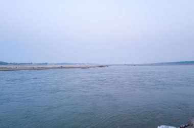 Hindistan 'ın Prayagraj kentindeki Sangam' da buluşan sakin Ganj ve Yamuna nehirlerinin geniş manzarası. Yumuşak gün ışığı ve sisli atmosfer akan sular ve uzak kumsallar üzerinde sakin bir hava yaratır..