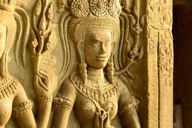 Angkor Vat, Kamboçya 'daki tapınak duvarında bir apsara dansçısının karmaşık kumtaşı oyması sıcak güneş ışığıyla aydınlatılır. Ayrıntılı Khmer rahatlama özellikleri süslü mücevherler, çiçek motifleri ve dokulu taş yüzeyler, sanatsal