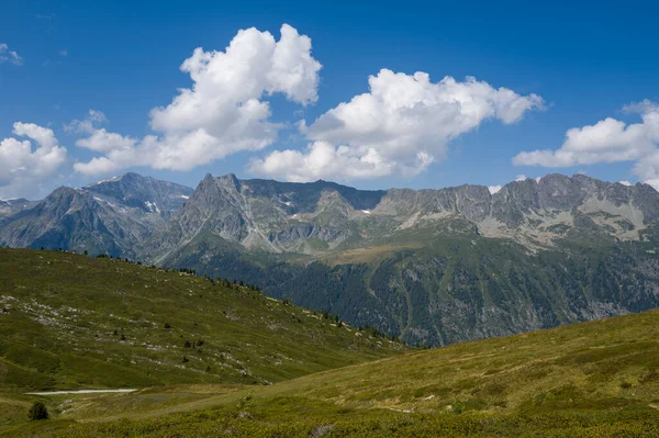 Yeşillik yeşil tepeler, Aiguillettes des Posettes bölgesinde kabarık beyaz bulutlarla kaplı parlak mavi gökyüzünün altında engebeli bir dağ sırasına doğru yavaşça yuvarlanıyor..