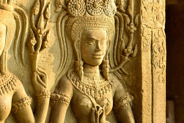 Angkor Vat, Kamboçya 'daki tapınak duvarında bir apsara dansçısının karmaşık kumtaşı oyması sıcak güneş ışığıyla aydınlatılır. Ayrıntılı Khmer rahatlama özellikleri süslü mücevherler, çiçek motifleri ve dokulu taş yüzeyler, sanatsal