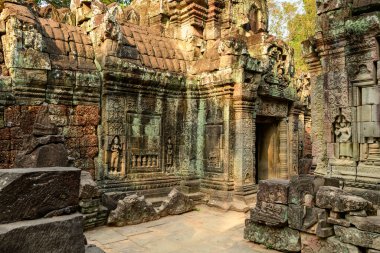 Ancient sandstone walls of Ta Som temple display intricate bas-reliefs and devata sculptures, illuminated by golden afternoon light in Cambodias Angkor region. Weathered masonry and scattered stones evoke centuries of Khmer heritage in a tranquil