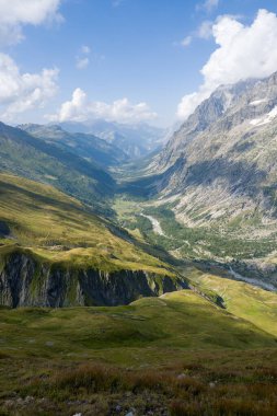 Val Ferret 'in yemyeşil yamaçları, engebeli kayalık uçurumları ve parlak mavi bir gökyüzünün altında kıvrımlı bir nehri kabarık bulutlarla süpürüyor..