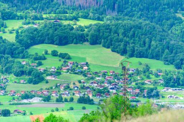 Passy, Haute-Savoie yakınlarındaki önde gelen bir elektrik direğinin yer aldığı gür yeşil alanlar ve sık ormanlarla çevrili kırsal bir köyün manzarası.