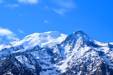 Mont Blanc ve Aiguille du Gouter 'ın karla kaplı tepeleri parlak mavi gökyüzüne karşı duruyor. Alp yamaçlarında parlak güneş ışığı, karmaşık dokuları açığa çıkarıyor..