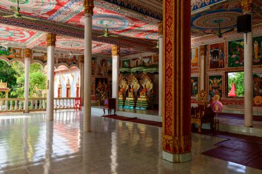 Vientiane, Laos 'ta geniş bir Budist tapınağı salonu, canlı anlatımsal resimler, karmaşık altın desenler ve renkli tavan tasarımları var. Doğal ışık, cilalı döşemeleri, beyaz sütunları ve özenle hazırlanmış heykelleri ön plana çıkarıyor.