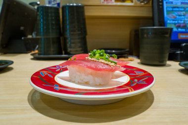 Sirkeli pirincin üzerinde taze ton balığı parçaları doğranmış yeşil soğan ve susam tohumlarıyla süslenmiş çağdaş bir Japon restoranında dekoratif kırmızı bir tabakta sunuluyor..