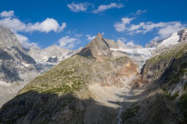 Engebeli dağların çarpıcı manzarası ve Val Ferret 'te kayalık yamaçlarla kaplı bir buzulun ve bulutlarla kaplı parlak mavi gökyüzünün altında dar bir akarsu..