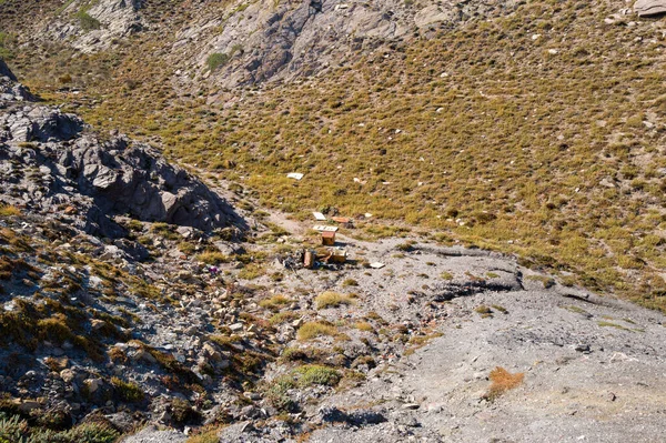 Arjantin yakınlarındaki çorak, güneşli, seyrek bitki örtüsü ve engebeli kayalarla kaplı bir yamaçta dağınık enkaz ve terk edilmiş bir araba görülebilir. Bu sert manzara çevresel ihmalleri vurguluyor ve doğal dokularla insan etkisinin çelişkisini vurguluyor..