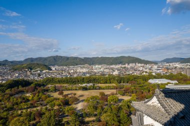 Himeji şehrinin geniş manzarası, yemyeşil parkı ve Himeji Kalesi 'nin tepelerinden görünen açık mavi gökyüzünün altındaki uzak yeşil tepeler..
