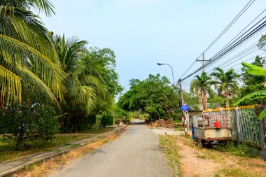 Güney Vietnam 'da Ben Tre, Mekong Delta' da sakin bir kırsal sokak, Hindistan cevizi palmiyeleri, muz bitkileri ve yoğun yeşillik ile çevrilidir. Sahnede basit bir kaldırım, elektrik kabloları, metal bir araba ve berrak bir köy atmosferi yer alıyor.