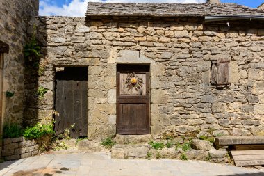 La Couvertoirade 'deki geleneksel taş kulübe cephesinde yaşlanmış ahşap kapılar, küçük bir kepenkli pencere ve kurumuş bir çiçek çelengi bulunuyor..