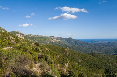 Sardinya 'nın Baunei ve Dorgali yakınlarındaki açık bir gökyüzünün altında engebeli yeşil tepeler ve kayalık yamaçlara bakan yüksek perspektifli bir bakış açısı. Güneş ışığı kıtır kıtır gölgeler oluşturur, doğal hatları ve vahşi bitkileri ortaya çıkarır..