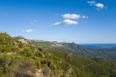 Sardinya 'nın Baunei ve Dorgali yakınlarındaki açık mavi gökyüzünün altında Akdeniz' e uzanan yeşil dağ yamaçları ve engebeli tepeler. Güneş ışığının vurgulanışı değişik dokular ve açık, doğal manzara.