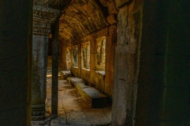 Yumuşak altın güneş ışığı, Angkor, Kamboçya 'daki Bayon Tapınağı' ndaki dokulu duvarları ve dar geçitleri aydınlatarak taş pencerelerden süzülüyor. Yıpranmış kumtaşı ve karmaşık oymalar sessiz bir tarihi çağrıştırıyor.