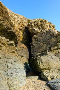 Cap de Carteret 'teki katmanlı uçurumları kesen dramatik bir kaya yarığının yakın görüntüsü parlak güneş ışığıyla aydınlanan parlak mavi gökyüzüne karşı. Engebeli taş dokuları ve toprak renkleri çarpıcı bir doğal bileşim yaratır..
