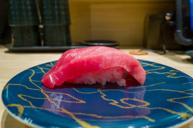 Tek bir parça taze orkinos nigiri, Osaka 'da modern bir suşi restoranında soyut altın çizgileri olan parlak mavi bir tabakta sunulan sirkeli pirincin üzerinde oturur..