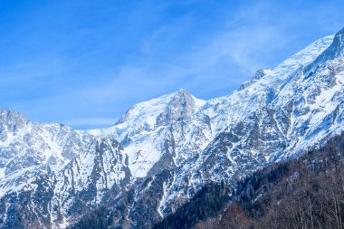 Karla kaplı yamaçlar ve Mont Blanc du Tacul 'un engebeli tepeleri, açık gün ışığıyla aydınlanan ve parlak mavi gökyüzüne karşı sertçe yükselir..