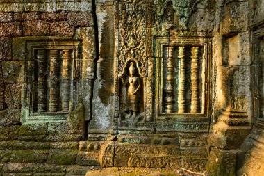 Angkor, Kamboçya 'daki Ta Nei Tapınağı' nın yıpranmış duvarında bir apara dansçısının karmaşık bas-rahatlaması ve ayrıntılı taş pencere kolları aydınlatılıyor. Antik Khmer duvar ustalığı ince oymalar, dokulu yüzeyler ve ince çizgiler ortaya çıkarır.