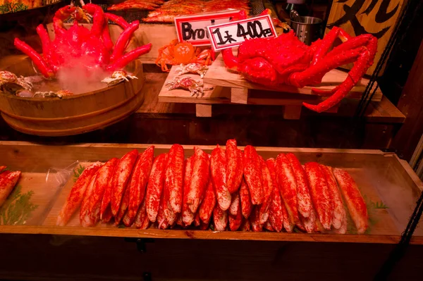 Canlı kırmızı yengeç bacakları Japonya 'nın orta Kyoto kentindeki hareketli bir gece yemeği standında ahşap bir tepside düzgünce dizilmiş. Ilık ışıklandırma taze deniz ürünlerini ve canlı pazar atmosferini geliştirir..
