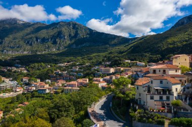 Maratea 'nın güneşli evleri ve yemyeşil dağlara kurulmuş terakotta çatıları olan manzarası. Dramatik gölgeler, canlı yapraklar ve berrak mavi bir gökyüzü sakin bir Akdeniz manzarası yaratır..