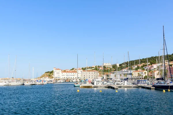 Bilinmeyen konum - 19 Haziran 2022: Görüntü açık mavi bir gökyüzünün altında, rıhtımda yüzen rıhtımlara yanaşmış çok sayıda yelkenli ve yatı olan, deniz kenarındaki konutları ve tepe kenarındaki evleri gösteren bir marina göstermektedir..