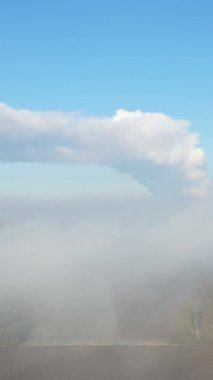 Dampierre, Fransa yakınlarındaki sisli kırsal bir arazide büyük beyaz buhar bulutu berrak mavi bir gökyüzüne yükselir. Kuşlar ön plandaki sisin içinden uçarak sakin ve atmosferik bir manzara yaratırlar..