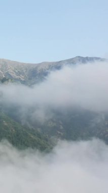 Pireneler 'deki yemyeşil dağların üzerinde bulutlar sürükleniyor, berrak bir gökyüzünün altında sakin ve atmosferik bir manzara yaratıyor..