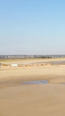 Plage de la Potiniere 'de berrak bir mavi gökyüzünün altında gelgit havuzları olan geniş kumlu sahil ufukta görünen uzak bir kasaba..