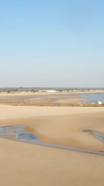 Geniş kumlu plaj gelgit havuzları ve açık mavi gökyüzü altında uzak evler Plage de la Potiniere, Fransa 'da. Barış dolu kıyı manzarası yaz ve seyahat kavramları için idealdir..
