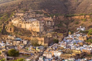 Bundi, Hindistan - 20 Mart 2022: Görüntü Garh Sarayı 'nın yoğun inşa edilmiş Bundi kentinin tepesinde yer aldığını, tepe boyunca uzanan geniş kale duvarları ve arka planda gün ışığı altında kuru tepeler olduğunu gösteriyor..