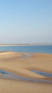 Fransa 'nın Plage de la Potiniere şehrinde gelgit havuzları ve berrak bir gökyüzü altında sakin mavi deniz ile geniş kumlu bir sahil. Barış dolu kıyı manzarası yaz ve seyahat kavramları için idealdir..