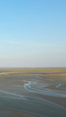 Fransa 'nın Le Mont-Saint-Michel kenti yakınlarındaki açık mavi gökyüzünün altındaki gelgit düzlükleri ve dolambaçlı su kanallarının geniş bir manzarası. Doğal desenler, bu sakin kıyı manzarasında çekilen gelgitle oluşur..