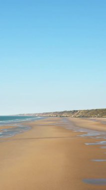 Omaha Sahili 'nin geniş manzarası. Altın kum, yumuşak dalgalar ve Fransa' nın Normandiya şehrinde açık mavi bir gökyüzü. Kıyı şeridi mesafeye kadar uzanıyor, barışçıl ve doğal bir deniz manzarası oluşturuyor..