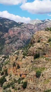 Korsika 'daki Porto Vadisi' nde parlak mavi bir gökyüzü altında dramatik kayalık kayalıklar ve yeşillikle kaplı engebeli dağlar. Çarpıcı jeolojik oluşumlara sahip doğal manzara.