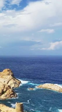 Korsika 'nın Fanale di Petra yakınlarında parçalı bulutlu bir gökyüzünün altında kayalık kıyı şeridi ve derin mavi denizin manzarası. Engebeli kayalar ve berrak okyanus dramatik bir deniz manzarası yaratır..