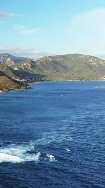 Sahil şeridinin ve dağların manzarası Les Iles Sanguinaires, Korsika, berrak mavi deniz ve engebeli arazi altında parlak bir gökyüzü.