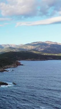 Mavi denizi ve uzak dağları olan engebeli bir kıyı şeridinin manzarası. Parçalı bulutlu bir gökyüzünün altında, Cargese, Korsika yakınlarında..