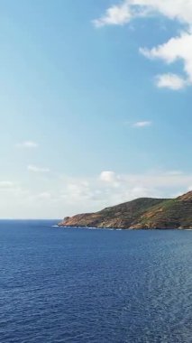 Korsika 'daki Delta du Fango' da açık bir gökyüzünün altında mavi deniz ve engebeli kıyı şeridi geniş. Uzak tepeleri ve sakin suları olan sakin Akdeniz manzarası.