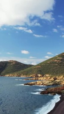 Delta du Fango, Korsika 'daki kayalık kıyı şeridi ve açık mavi denizin manzarası. Parlak bir gökyüzünün altında dağınık bulutlar var..