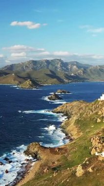 Les Iles Sanguinaires, Korsika 'daki engebeli kıyı şeridi ve turkuaz suların dramatik manzarası, mavi gökyüzünün altındaki kayalara çarpan dalgalar..