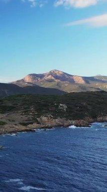 Korsika, Cargese yakınlarındaki engebeli kıyı şeridi ve dağların manzarası, açık mavi bir gökyüzünün altında. Görüntü, Akdeniz kıyılarının doğal güzelliklerini yansıtıyor..
