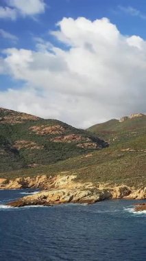Korsika 'daki Delta du Fango' daki engebeli kıyı şeridi ve tepelerin manzarası berrak mavi su ve dramatik bulutlarla kaplı..
