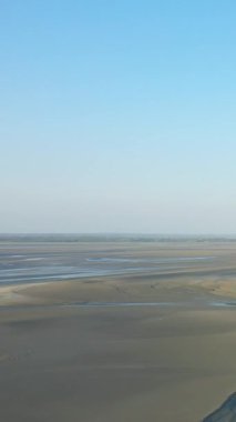 Fransa 'nın Le Mont-Saint-Michel şehrinde açık mavi bir gökyüzünün altındaki kumlu gelgit düzlüklerinin geniş manzarası. Doğal dokuları ve yumuşak ışığı olan minimalist bir manzara..