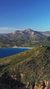 Engebeli dağların manzarası ve parlak bir gökyüzünün altında berrak mavi suyla dolu gür bir kıyı şeridi. Akdeniz ortamında doğal güzellik ve sükunet.