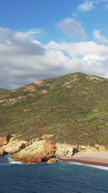 Delta du Fango, Korsika 'da bulutlu bir gökyüzünün altında yeşil tepeleri ve mavi denizi olan kayalık bir sahil manzarası..