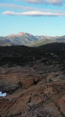 Korsika, Cargese yakınlarında açık mavi gökyüzünün altında kayalık arazisi ve uzak dağları olan engebeli bir kıyı şeridi. Doğal manzara Akdeniz bölgesinin vahşi güzelliğini vurguluyor..
