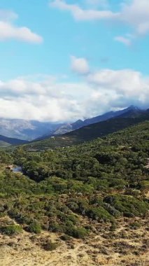 Fransa, Korsika 'da bulutlu mavi gökyüzü altında yemyeşil, dolambaçlı nehir ve uzak dağlarla Delta du Fango manzarası.