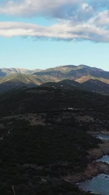 Korsika, Cargese yakınlarında bulutlu bir gökyüzünün altında kayan tepelerin ve engebeli dağların manzarası. Kıyı kayalıkları ve yemyeşil bitkileri olan doğal arazi..